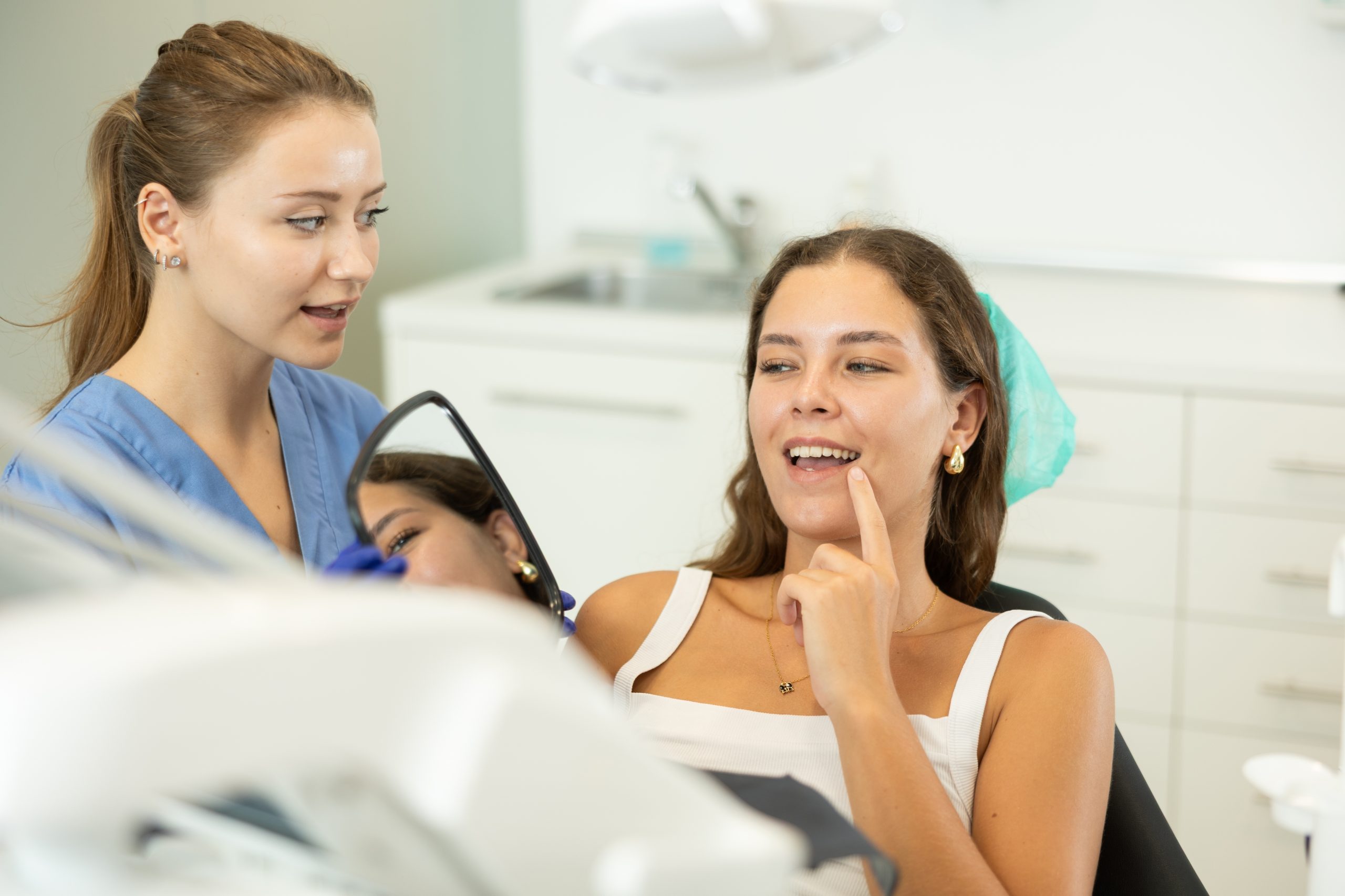 Dental hygienist in blue scrubs discussing treatment with patient in dental chair