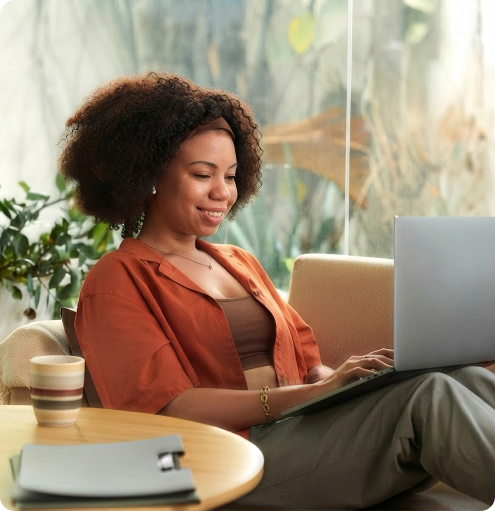 Woman smiling while using a laptop on a sofa during a telehealth session