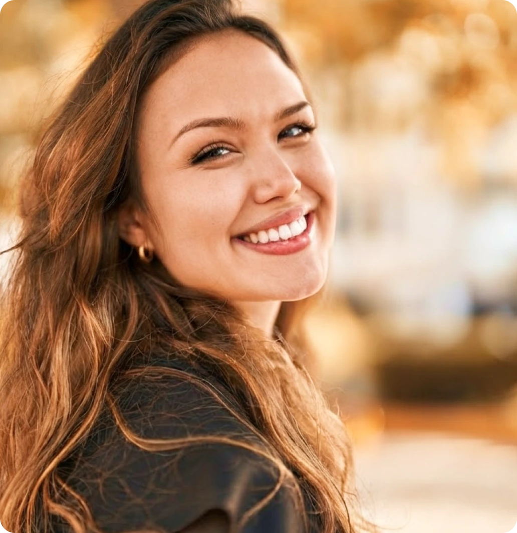Smiling woman with wavy hair standing outdoors at golden hour