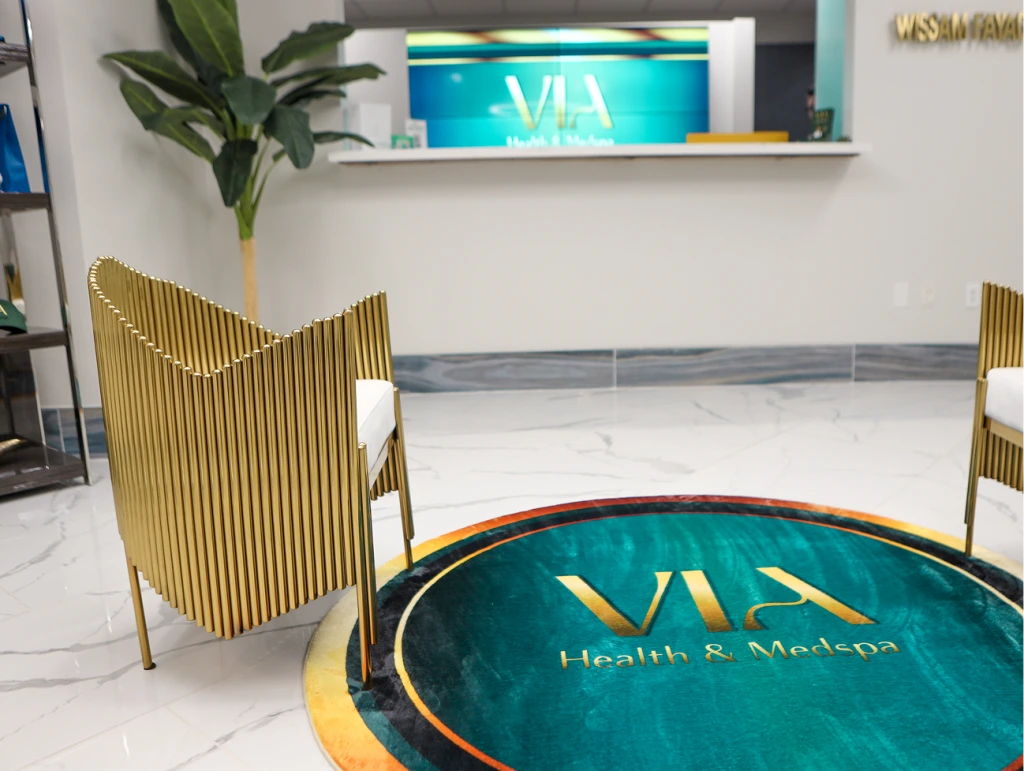 VIA Health & Medspa reception area with marble floor, gold-ribbed chairs, and turquoise branded signage on white shelf