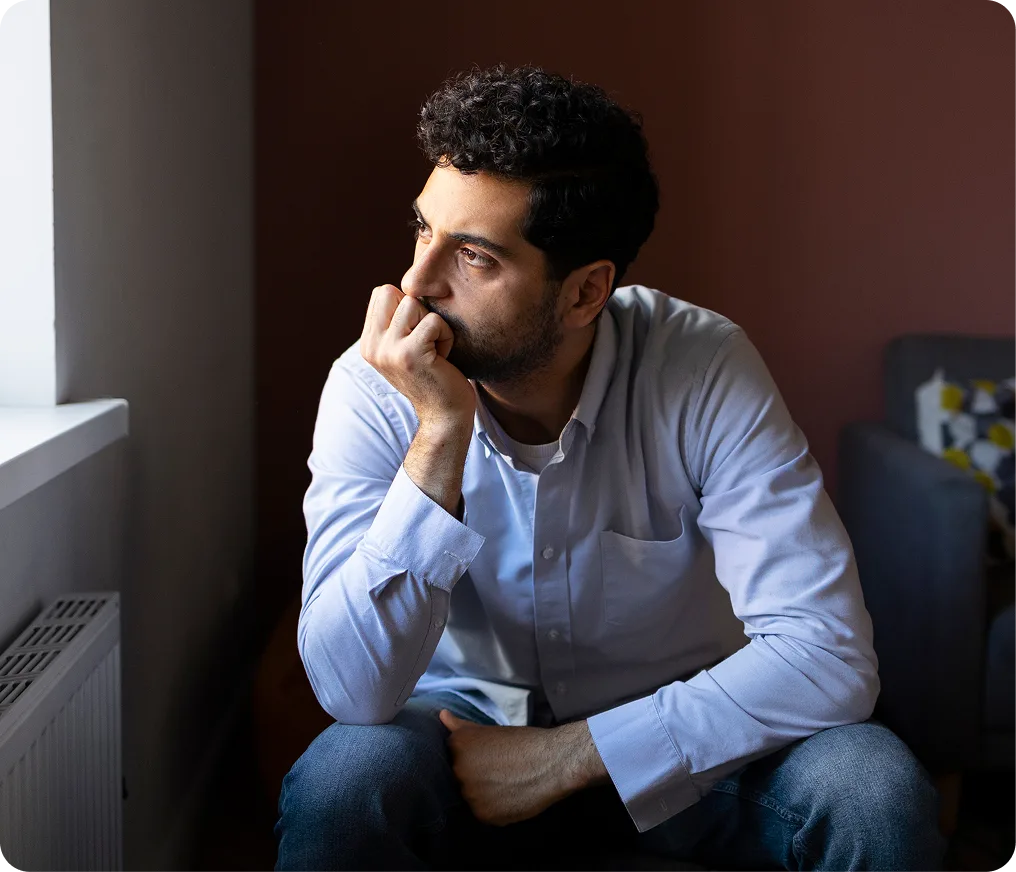 Man in blue shirt sitting pensively with hand to face against brown wall
