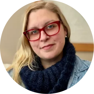 Woman wearing red glasses and dark blue scarf, smiling at the camera