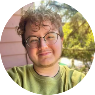 Person with curly hair and glasses wearing yellow-green shirt, outdoor background