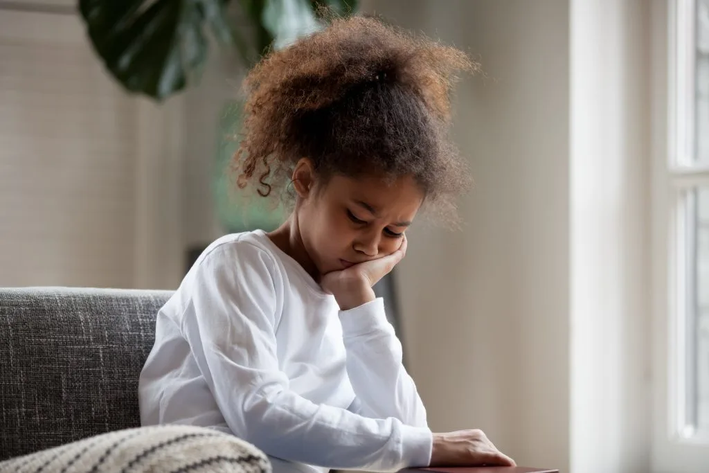 Young child resting chin on hand with sad expression sitting on couch