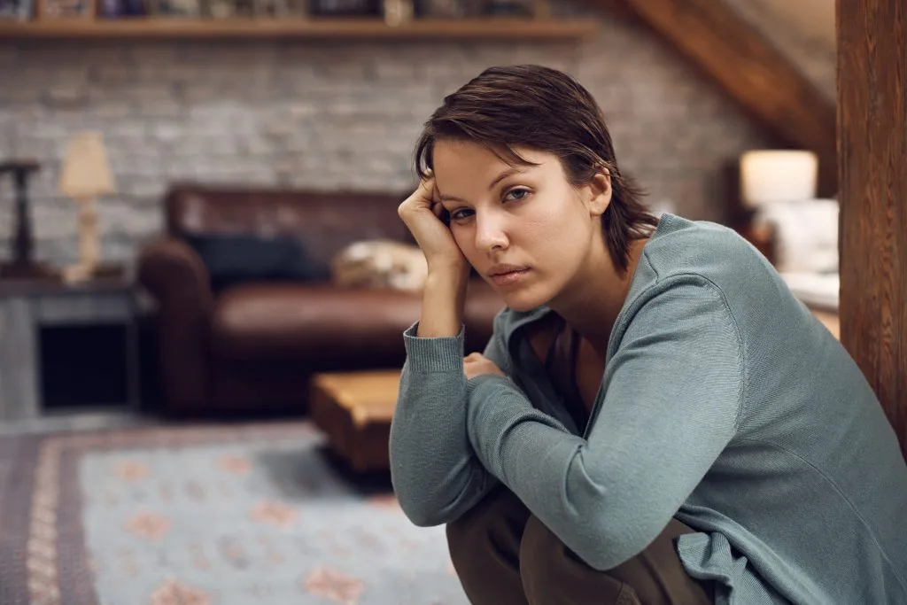 Woman with troubled expression sits alone in modern living room