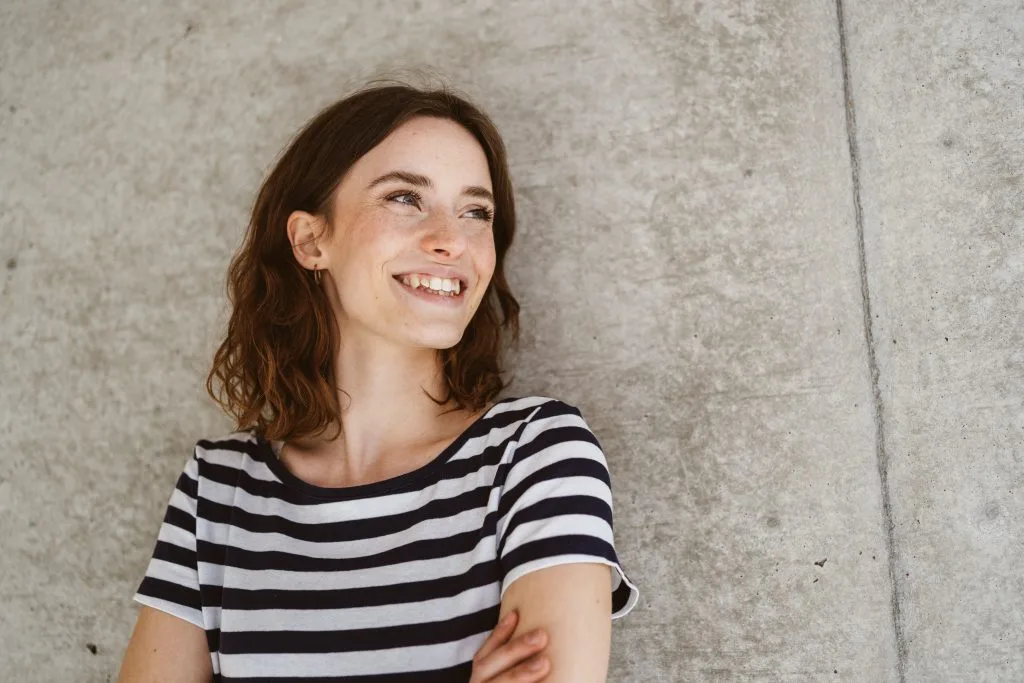 Young woman in black and white striped shirt laughing against concrete wall