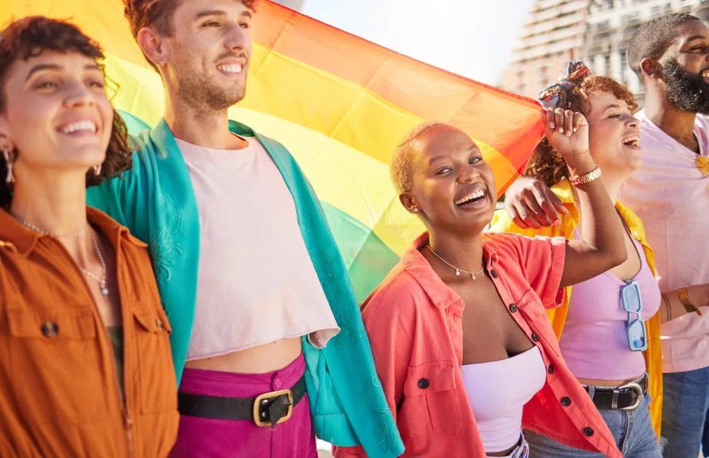 Group of diverse people smiling while holding a rainbow pride flag outdoors