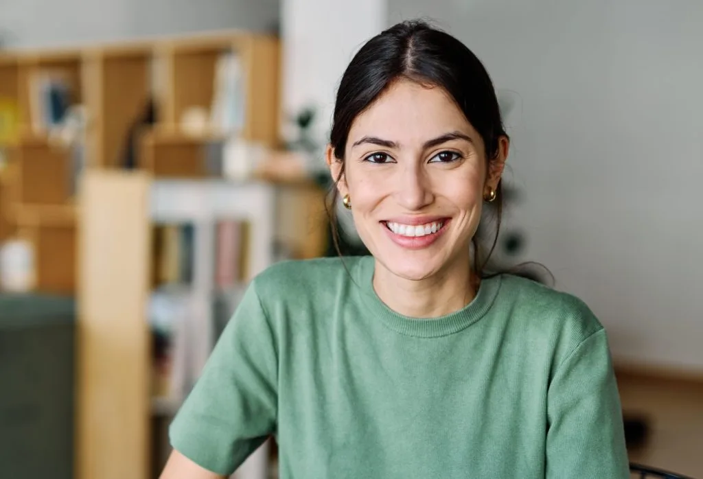 Woman in green shirt smiling in bright therapy clinic interior with wooden shelving