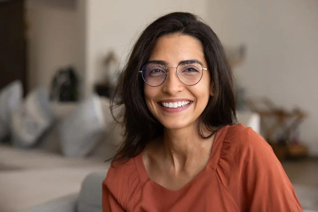 Woman wearing glasses smiling at camera in a bright indoor space
