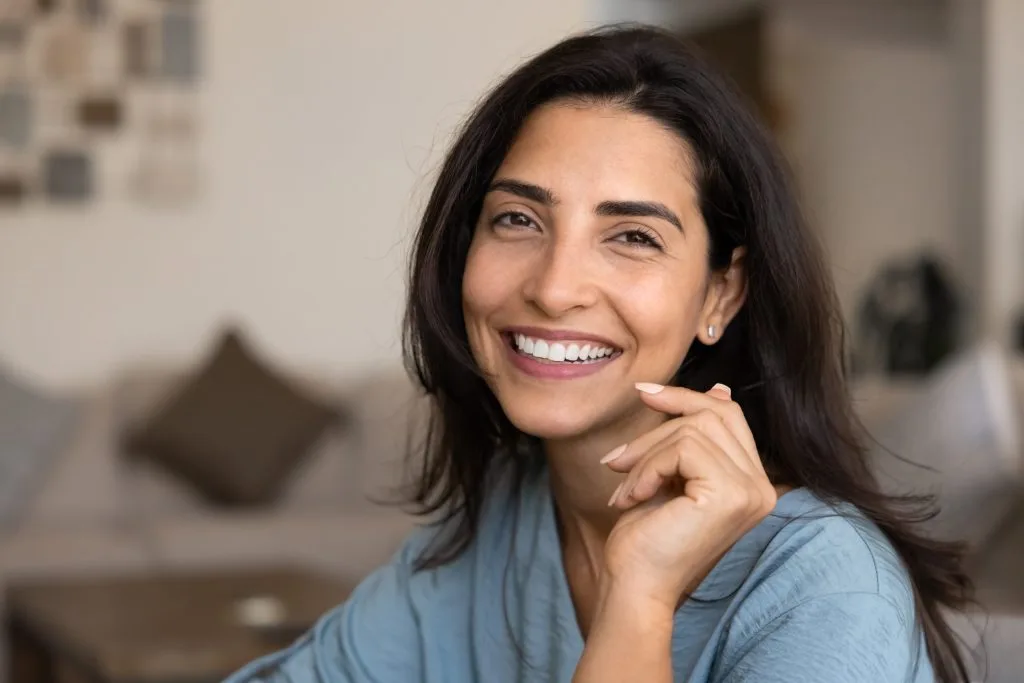 Woman with dark hair smiling with hand near face in modern clinical setting