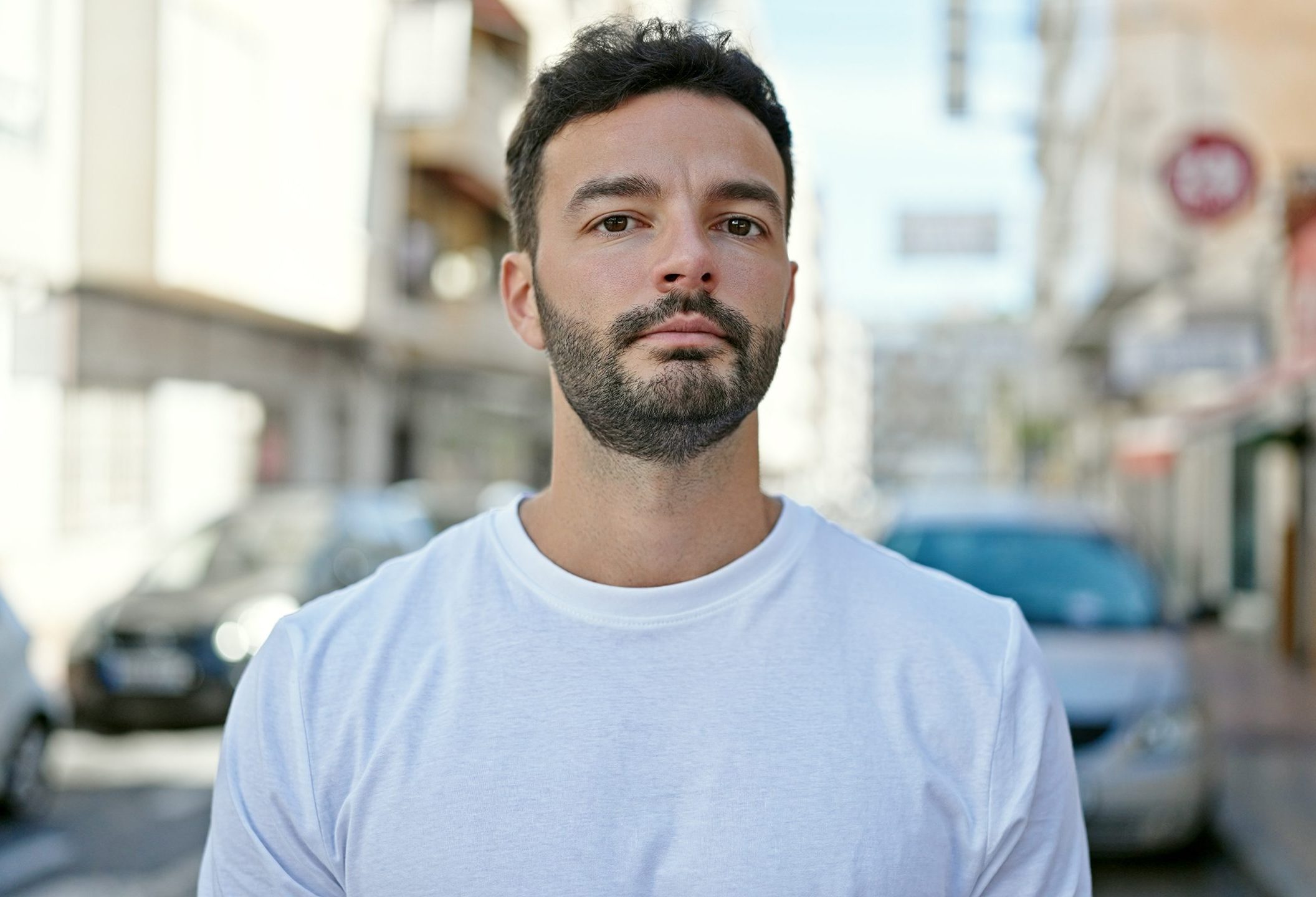 Young Hispanic man standing on a street with a serious expression – social anxiety treatment patient