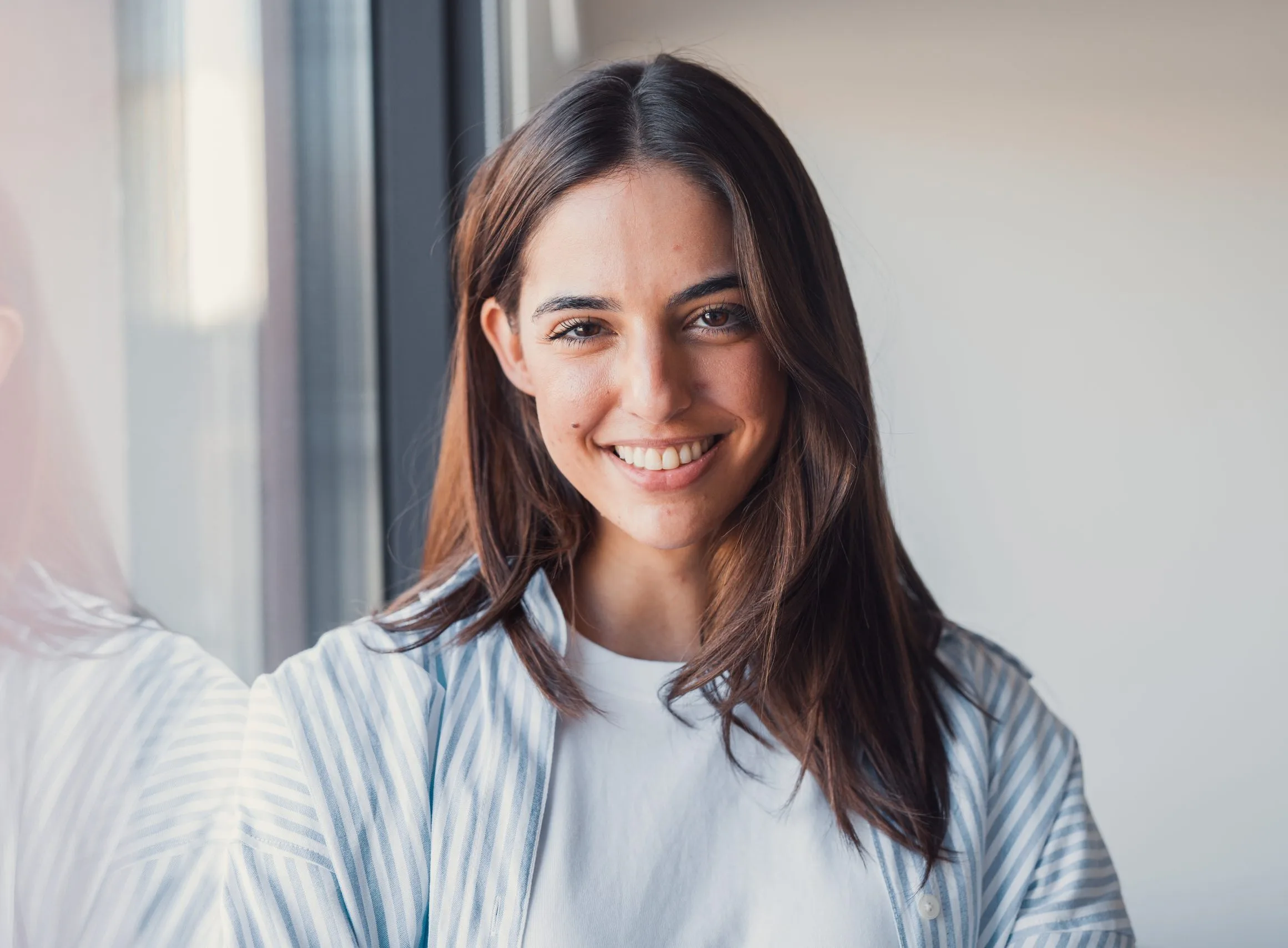 Smiling young woman standing by a window – psychiatric evaluation patient