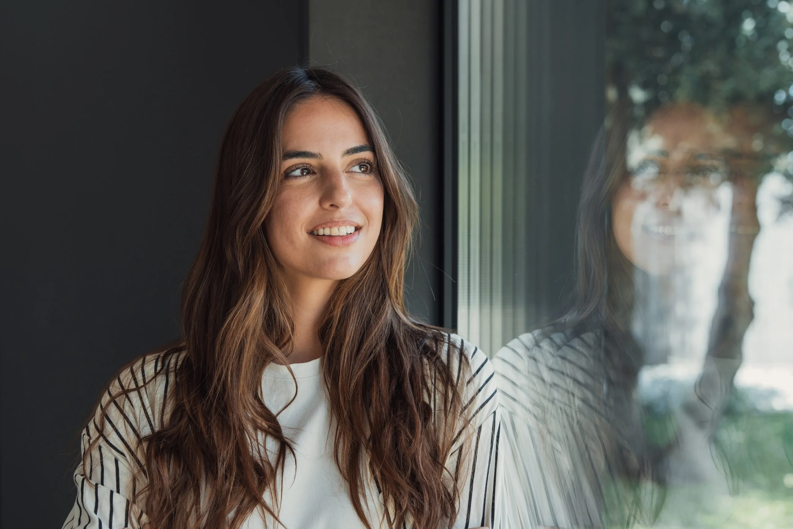 Young woman smiling thoughtfully while looking out a window – psychiatrist in Dublin, CA