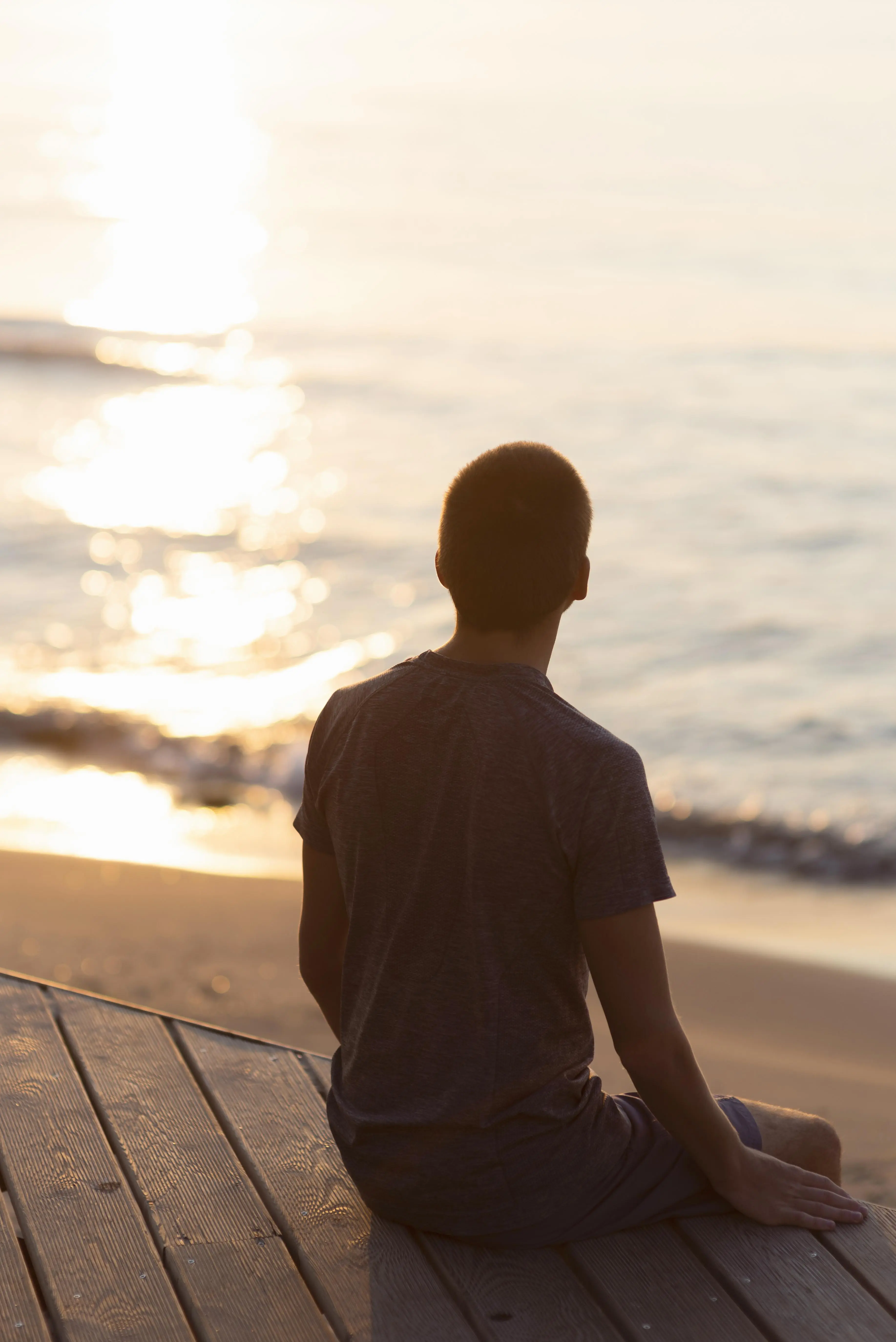 Man meditating on the beach, viewed from behind