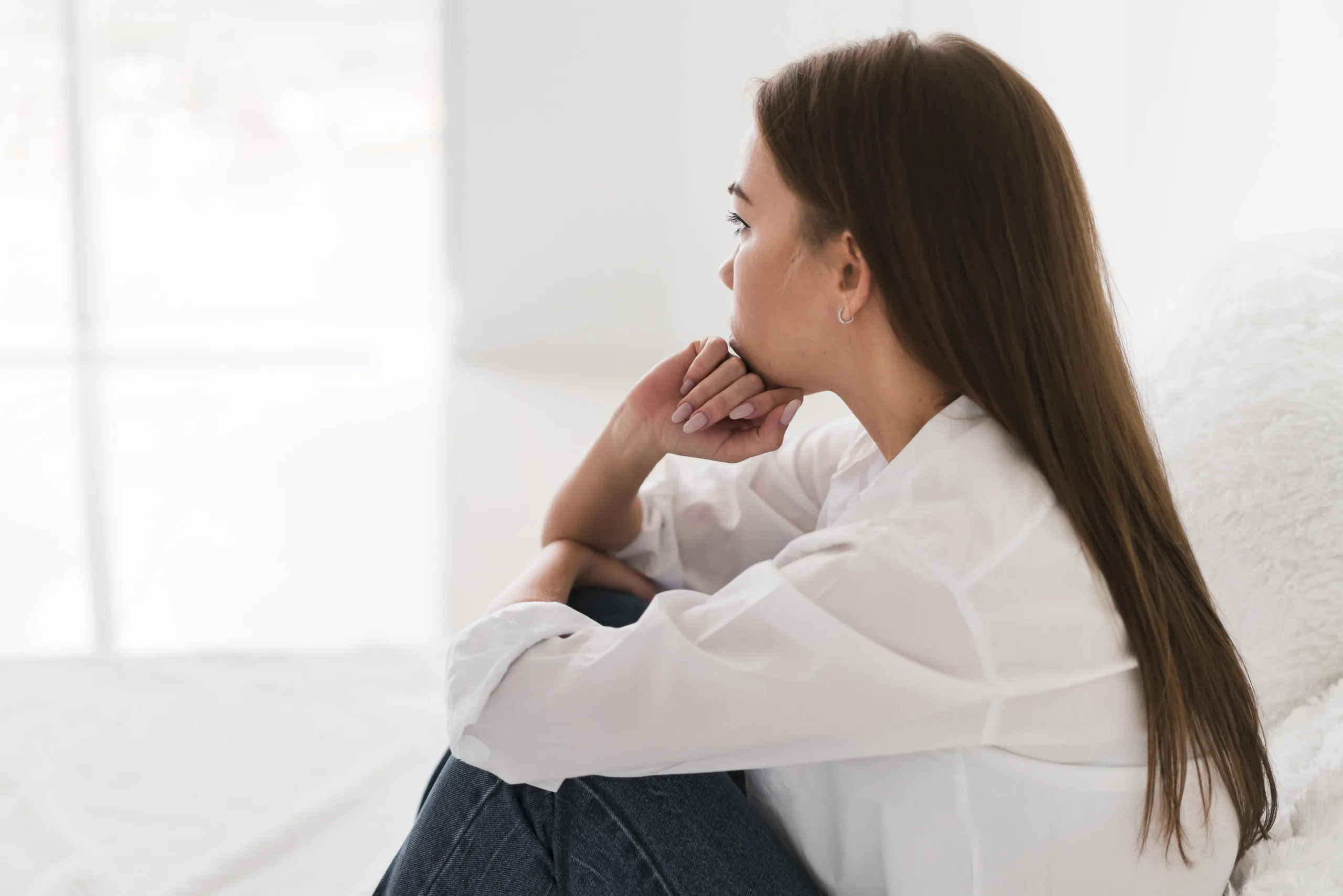 Woman sitting alone indoors with hand to chin, looking thoughtful or concerned