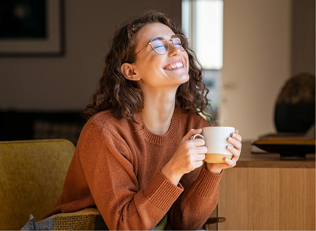 Woman in rust sweater holding mug, looking upward contentedly while seated
