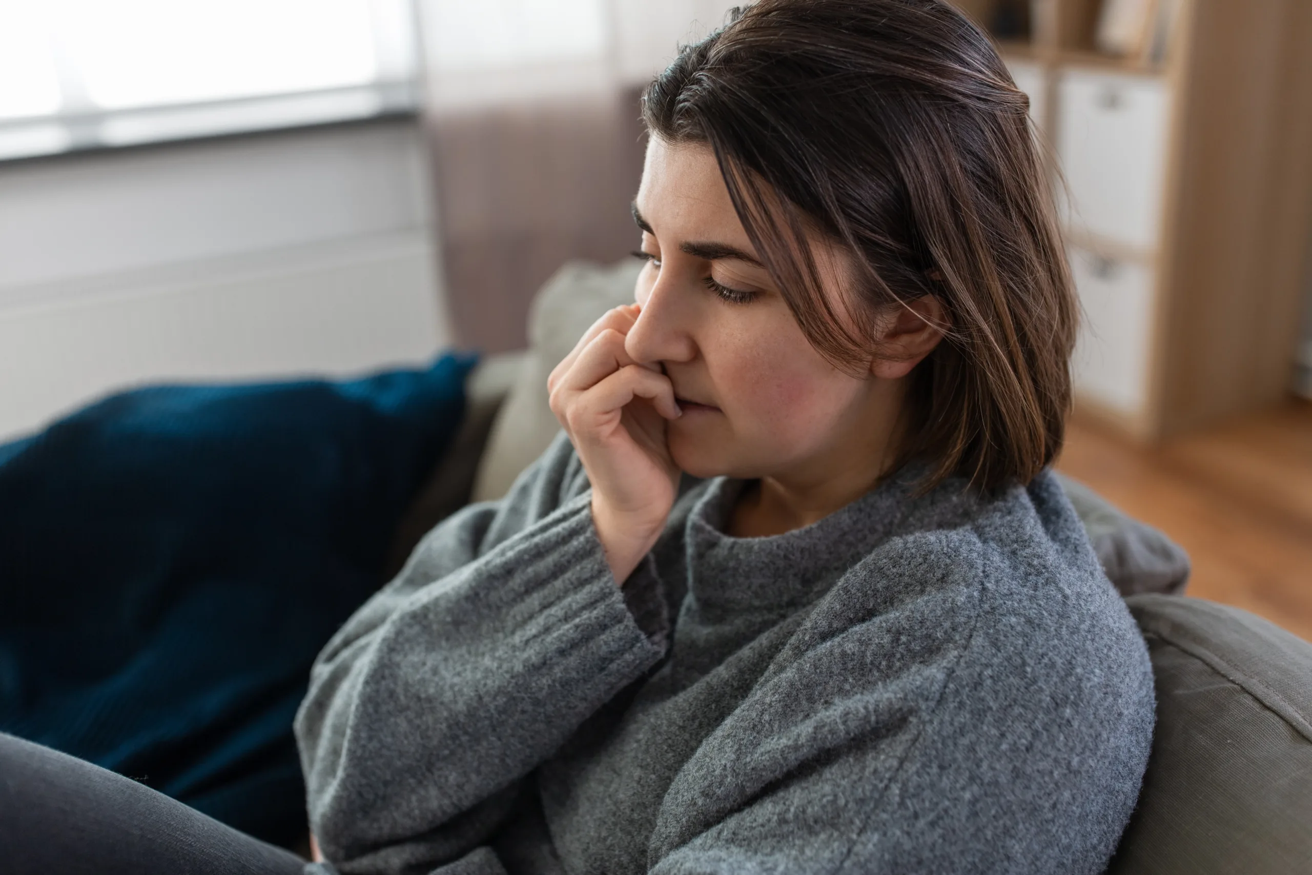 Woman sitting on a sofa at home with a troubled expression, hand to face