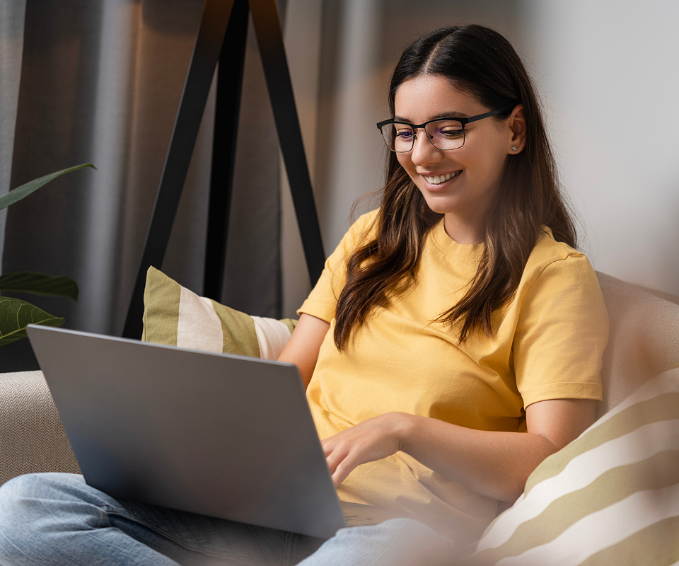 Woman in yellow shirt smiling while using laptop at home on couch