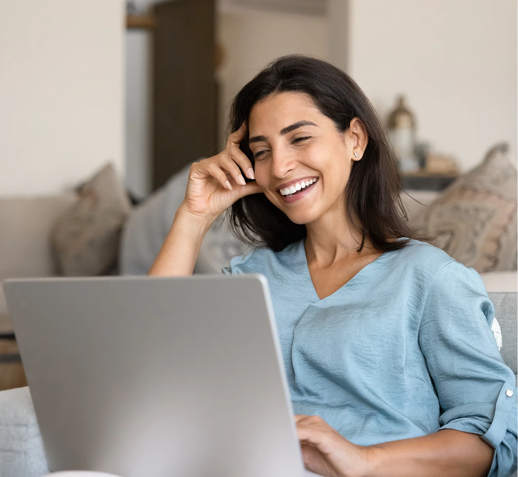 Woman in light blue shirt smiling during virtual therapy session on laptop