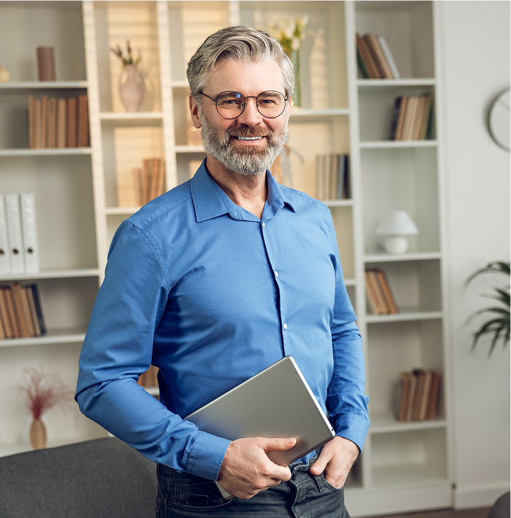 Man in blue shirt holding tablet smiling in office with bookshelves