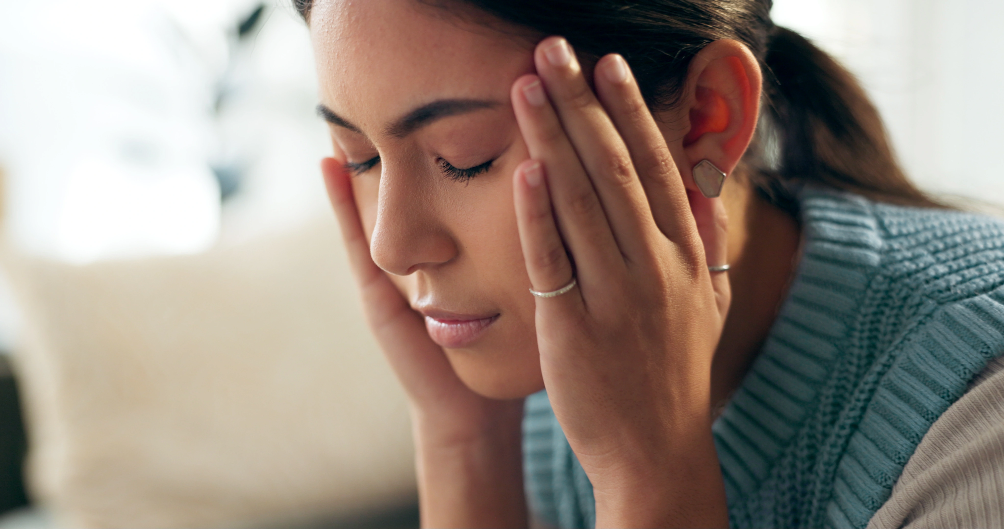 Woman on a couch at home with a stress headache, eyes closed