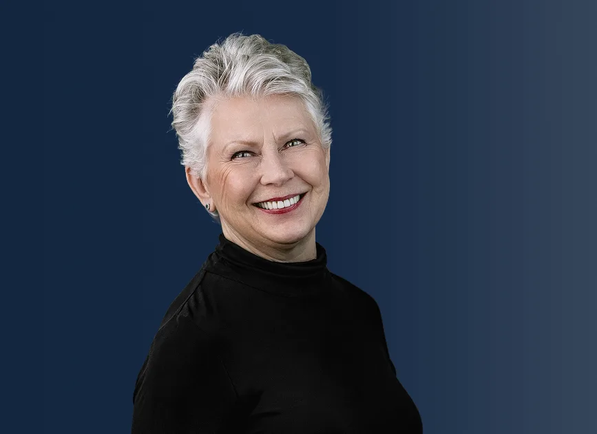 Smiling woman with white hair wearing black turtleneck against blue background