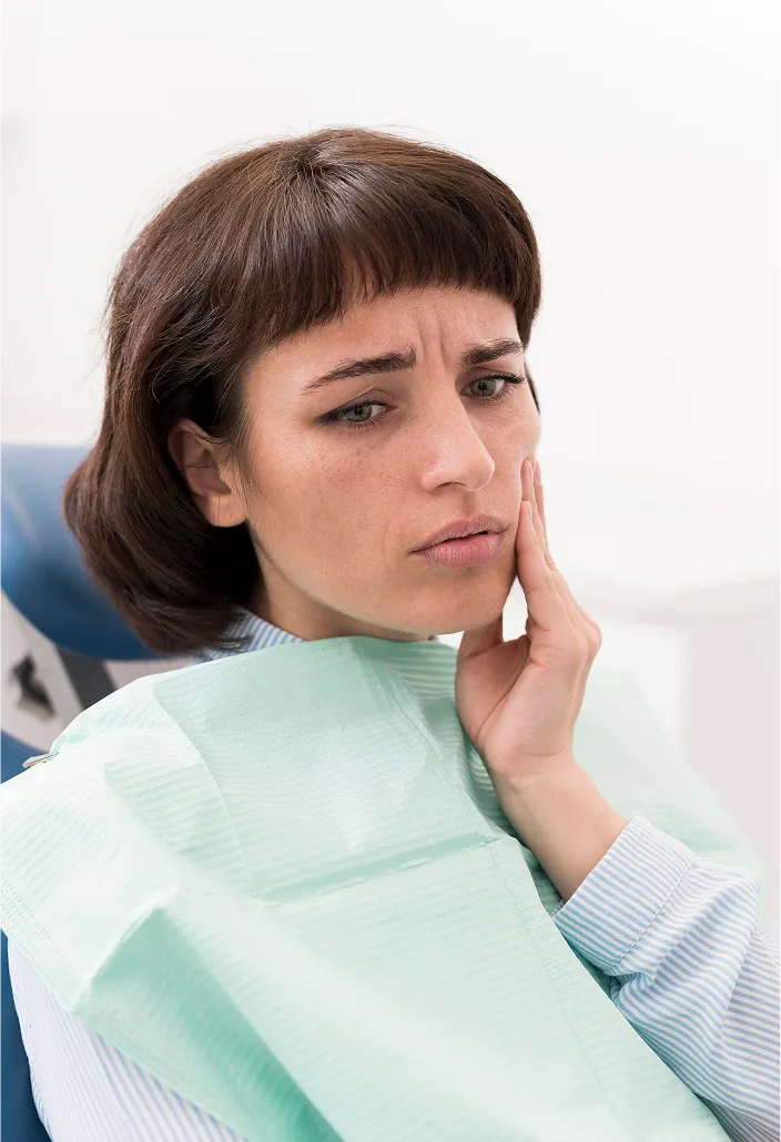 Woman in dental bib touching her cheek with an uncomfortable expression