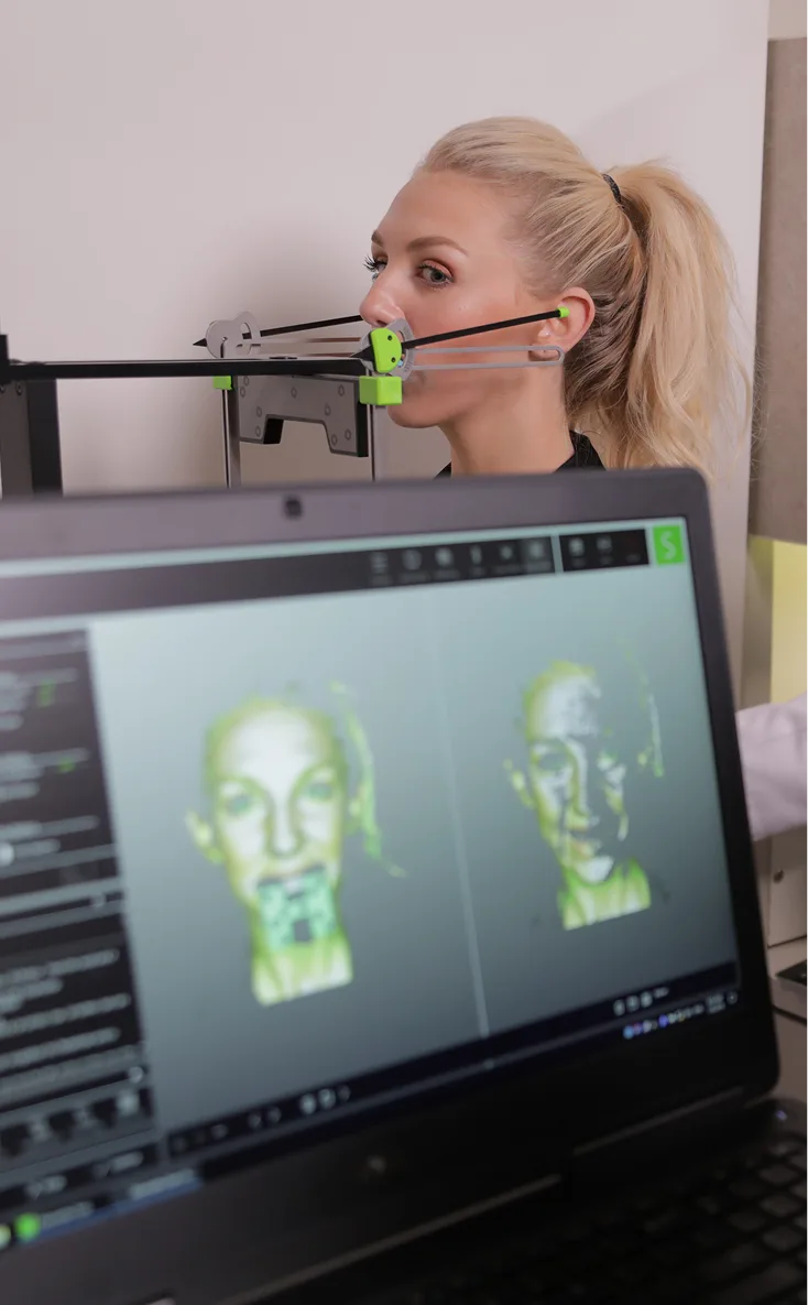 Woman wearing 3D facial mapping device while viewing thermal scan images on computer screen