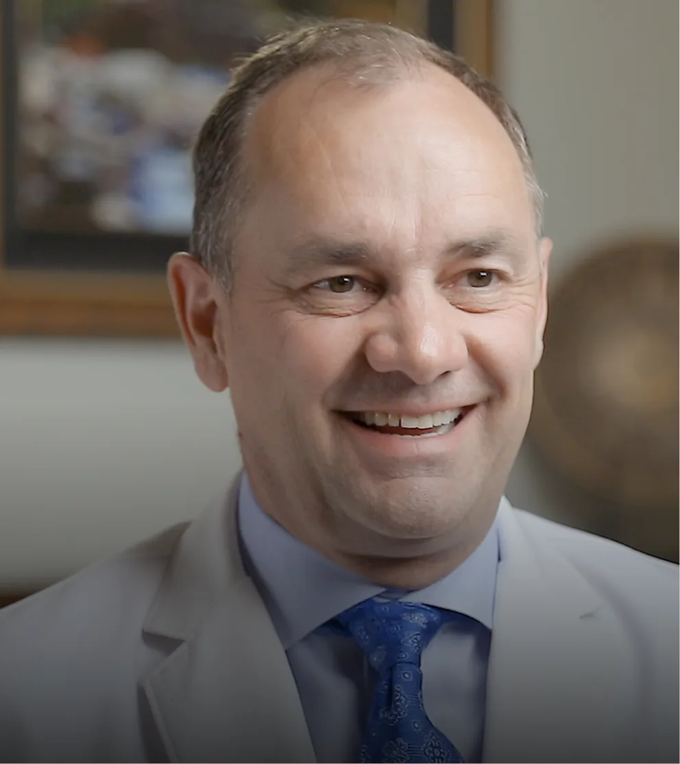 Dental professional in light gray suit and blue tie smiling in office setting