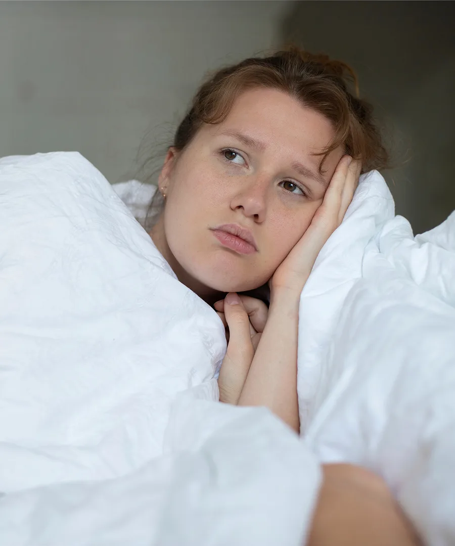 Woman in bed appearing uncomfortable, holding her face and jaw in pain