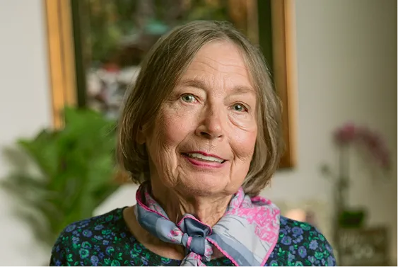 Older woman with gray hair smiling at camera in home setting with plants