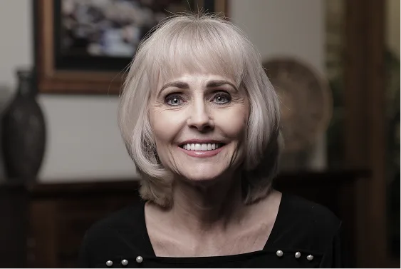 Older woman with white bob haircut smiling at camera indoors
