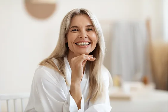 Woman with blonde hair smiling with hand near face in bright indoor setting