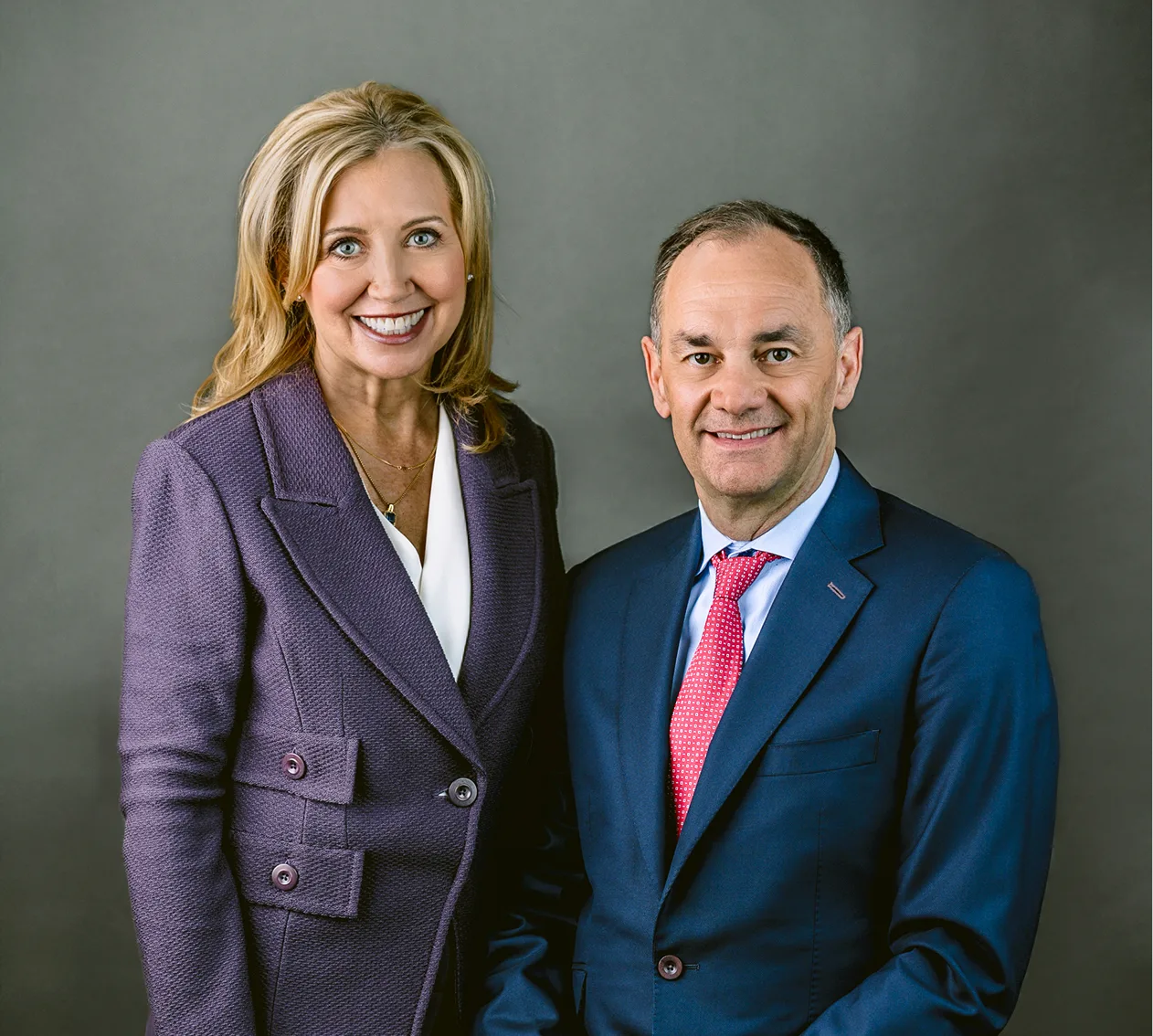 Woman in purple blazer and man in blue suit posing together for professional portrait