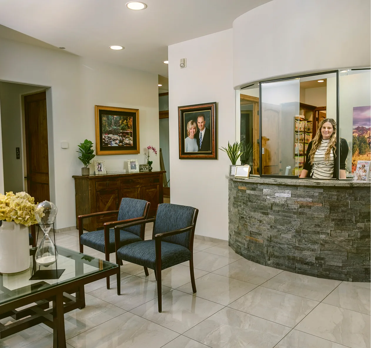 Dental practice reception area with reception desk, waiting chairs, framed photos, and floral arrangements