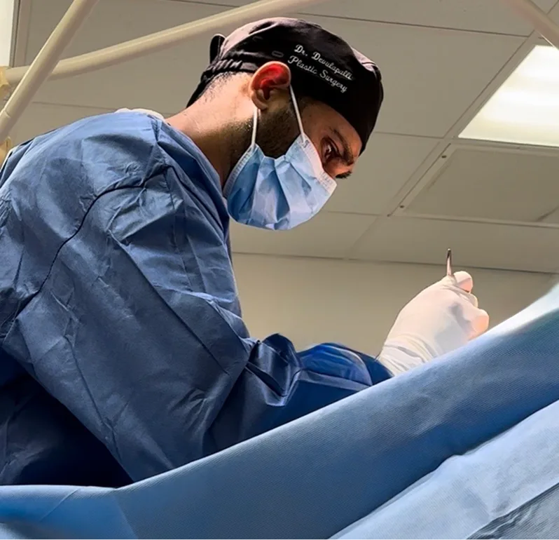 Surgeon in blue scrubs and surgical mask performing procedure on patient