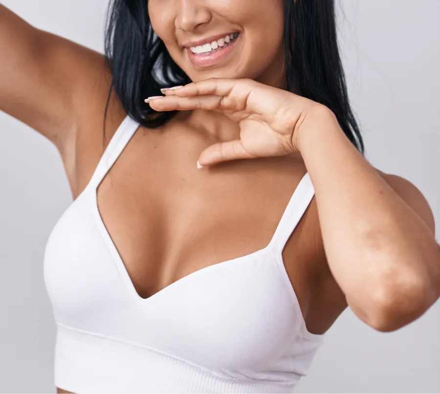 Smiling woman in white bikini top with arms raised, touching shoulder and displaying chest area