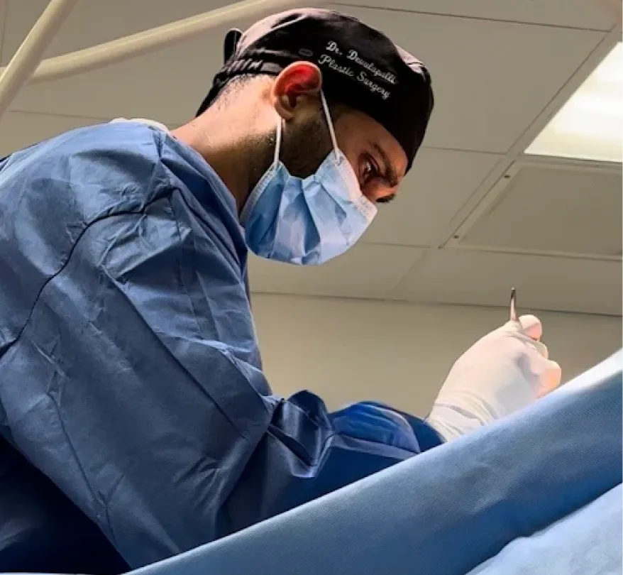 Plastic surgeon in surgical cap, mask, and blue scrubs performing procedure