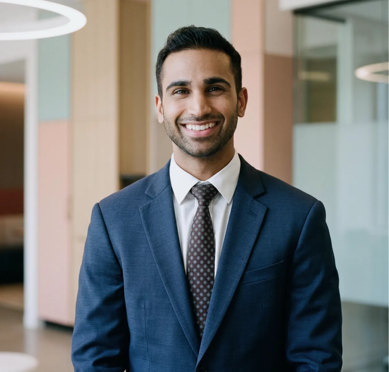 Man in dark blue blazer and burgundy tie smiling in modern medical office
