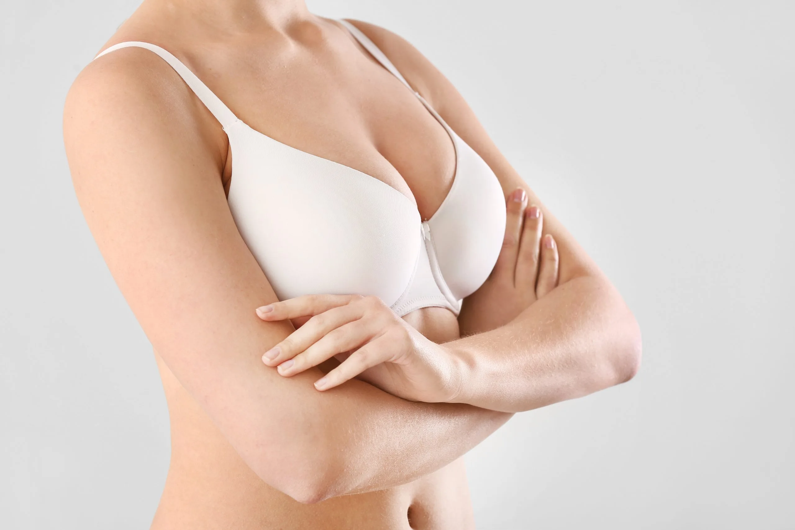 Woman in white bra with arms crossed, viewing breast profile from side angle