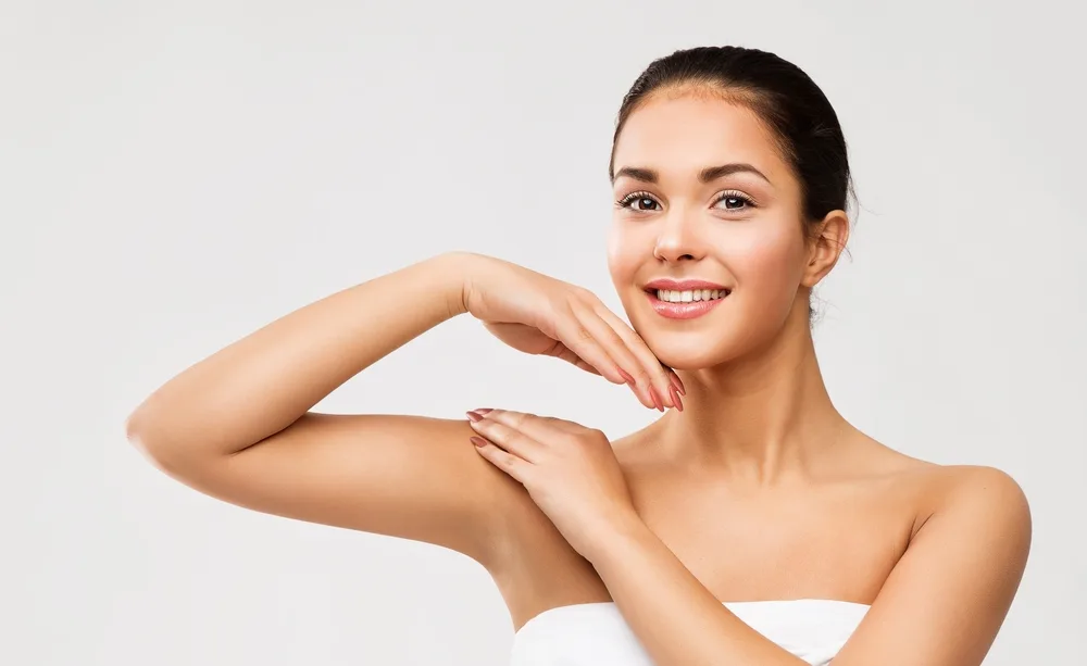 Smiling woman touching her face, displaying clear, healthy skin