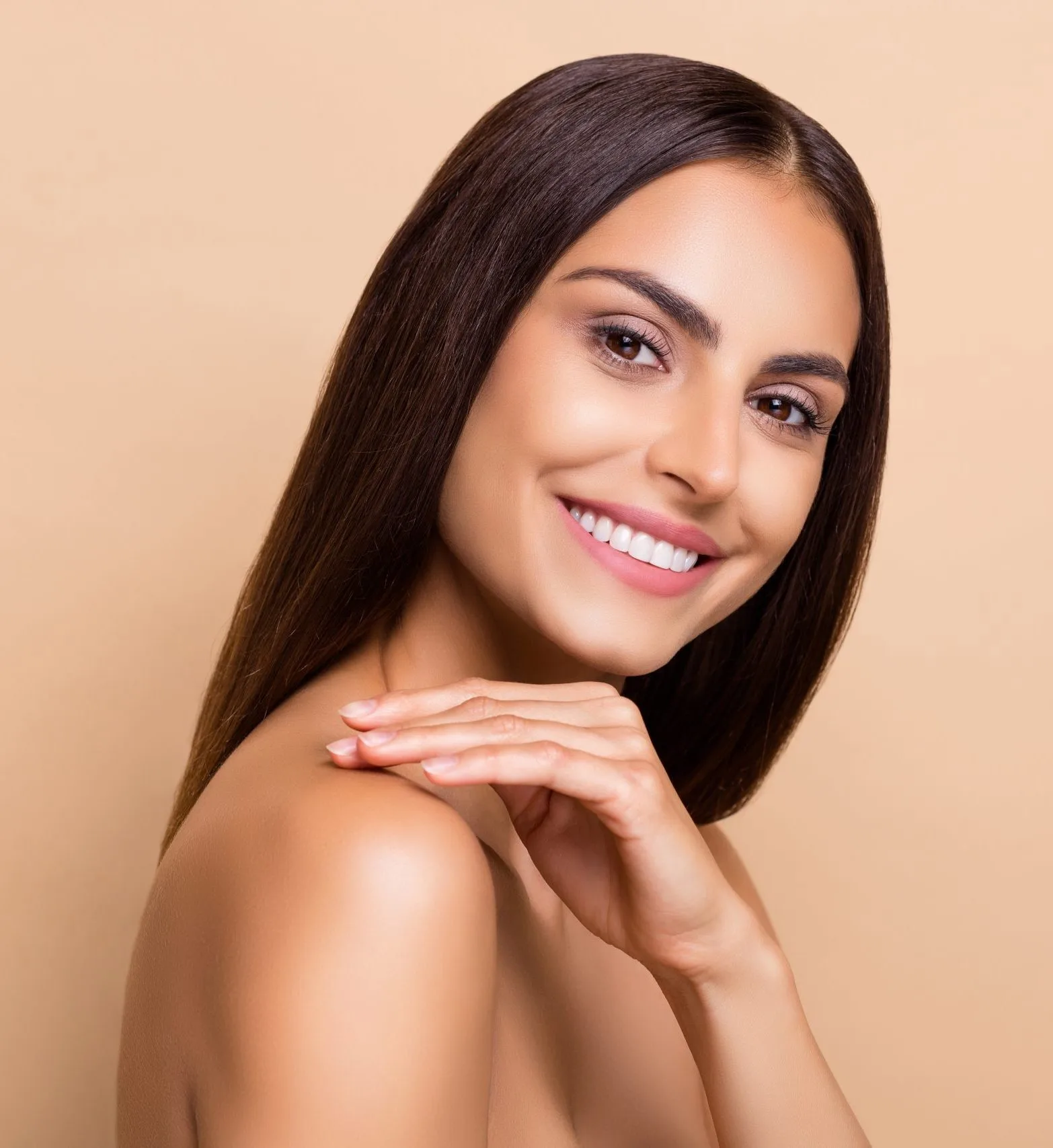 Woman smiling at camera, touching shoulder, displaying clear skin and teeth