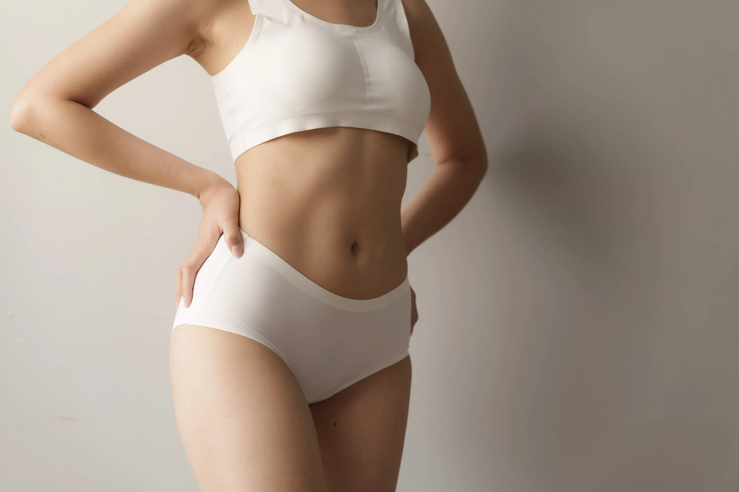 Woman in white crop top and briefs with hand on hip, showing defined midsection