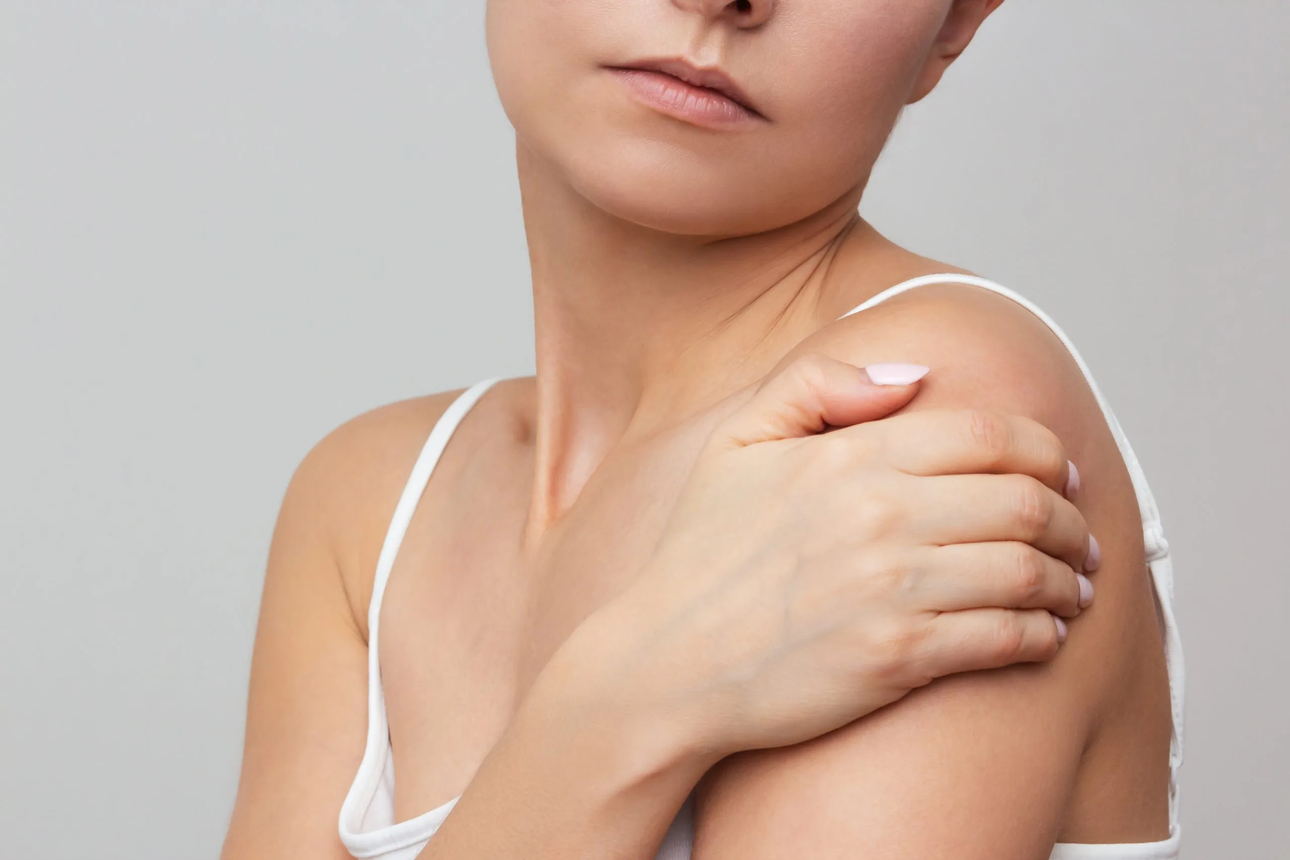 Woman touching shoulder and neck area, showing jaw and collarbone definition