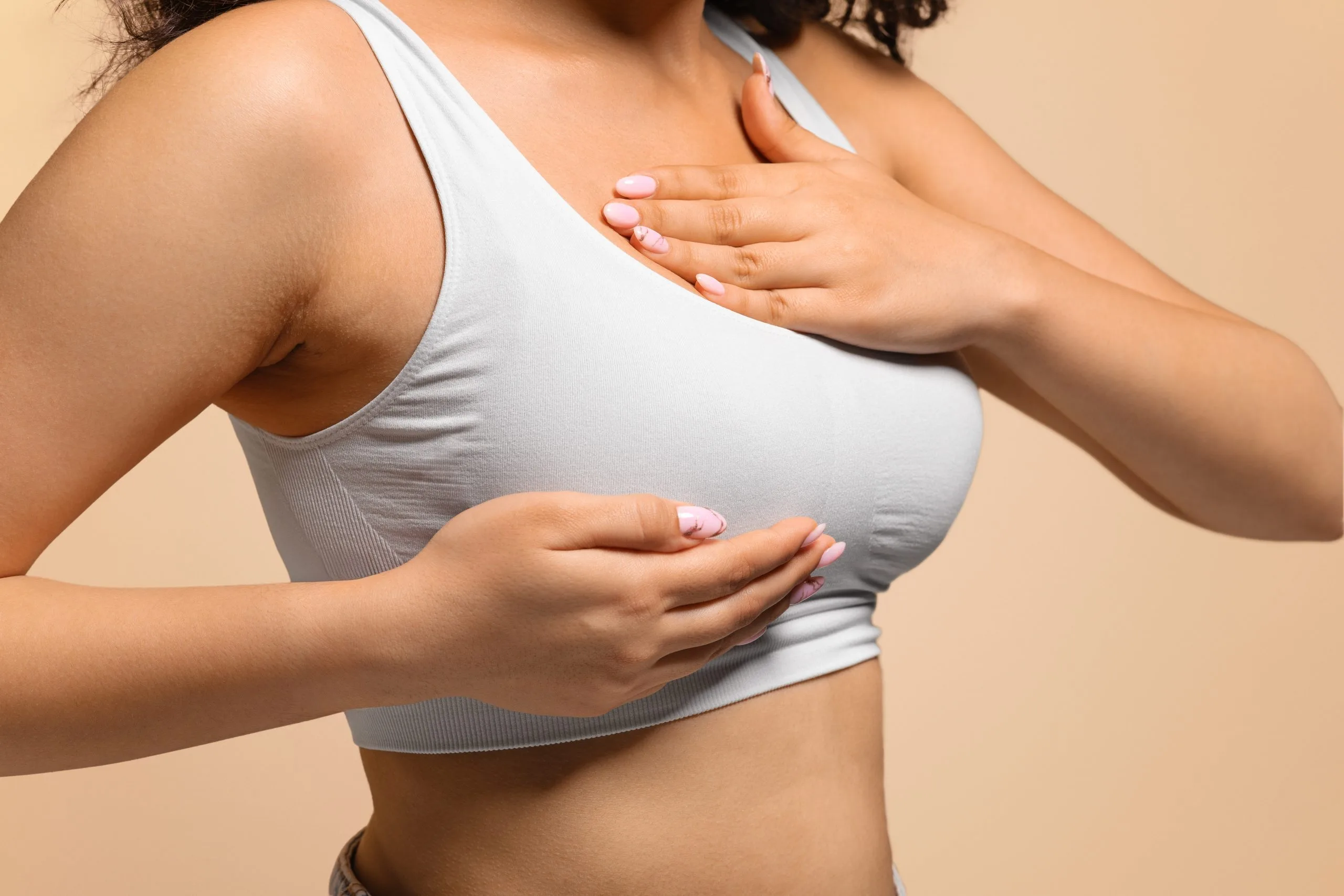 Woman in white sports bra palpating breast tissue with both hands