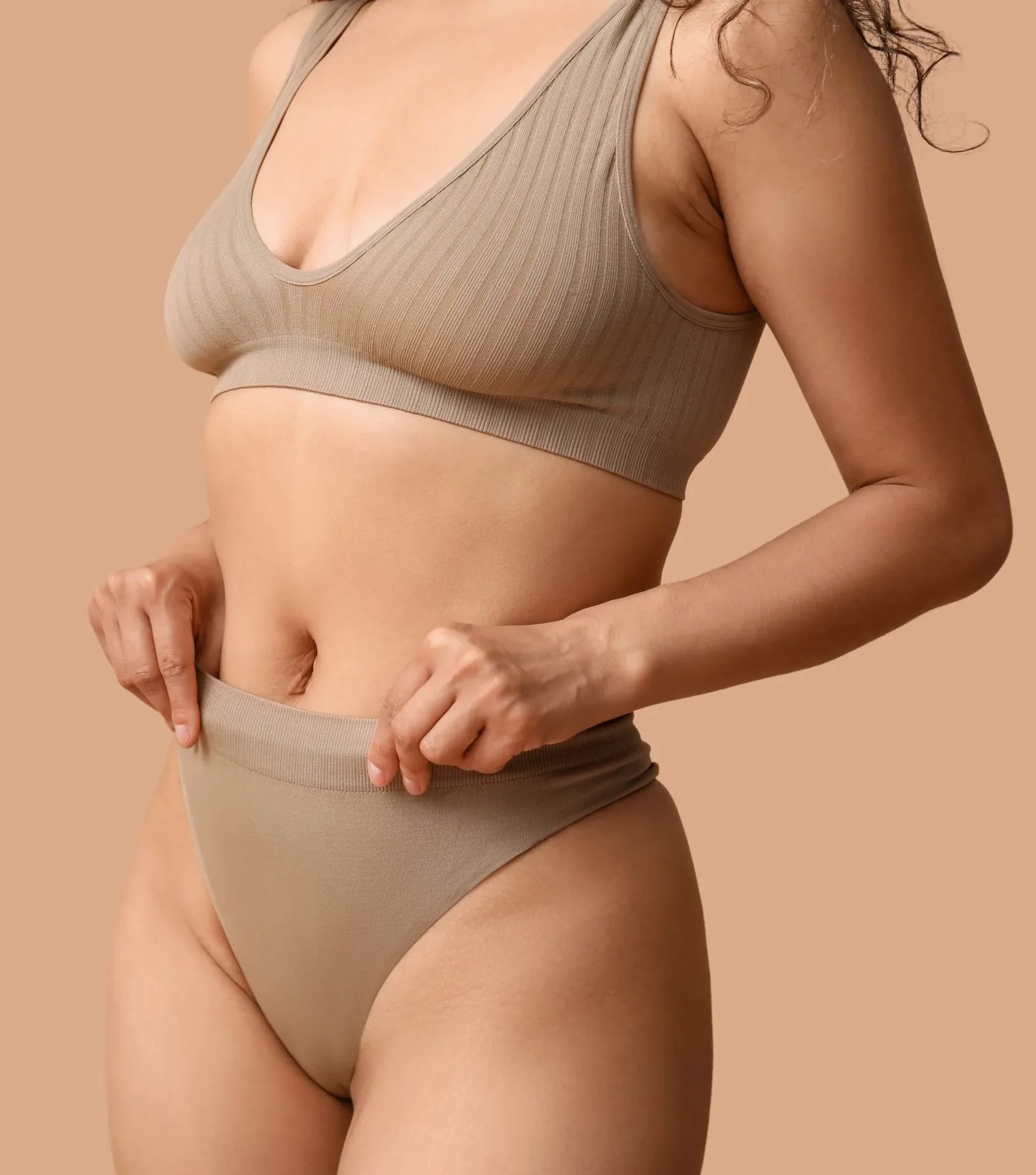 Woman in beige sports bra pinching abdominal skin to show elasticity