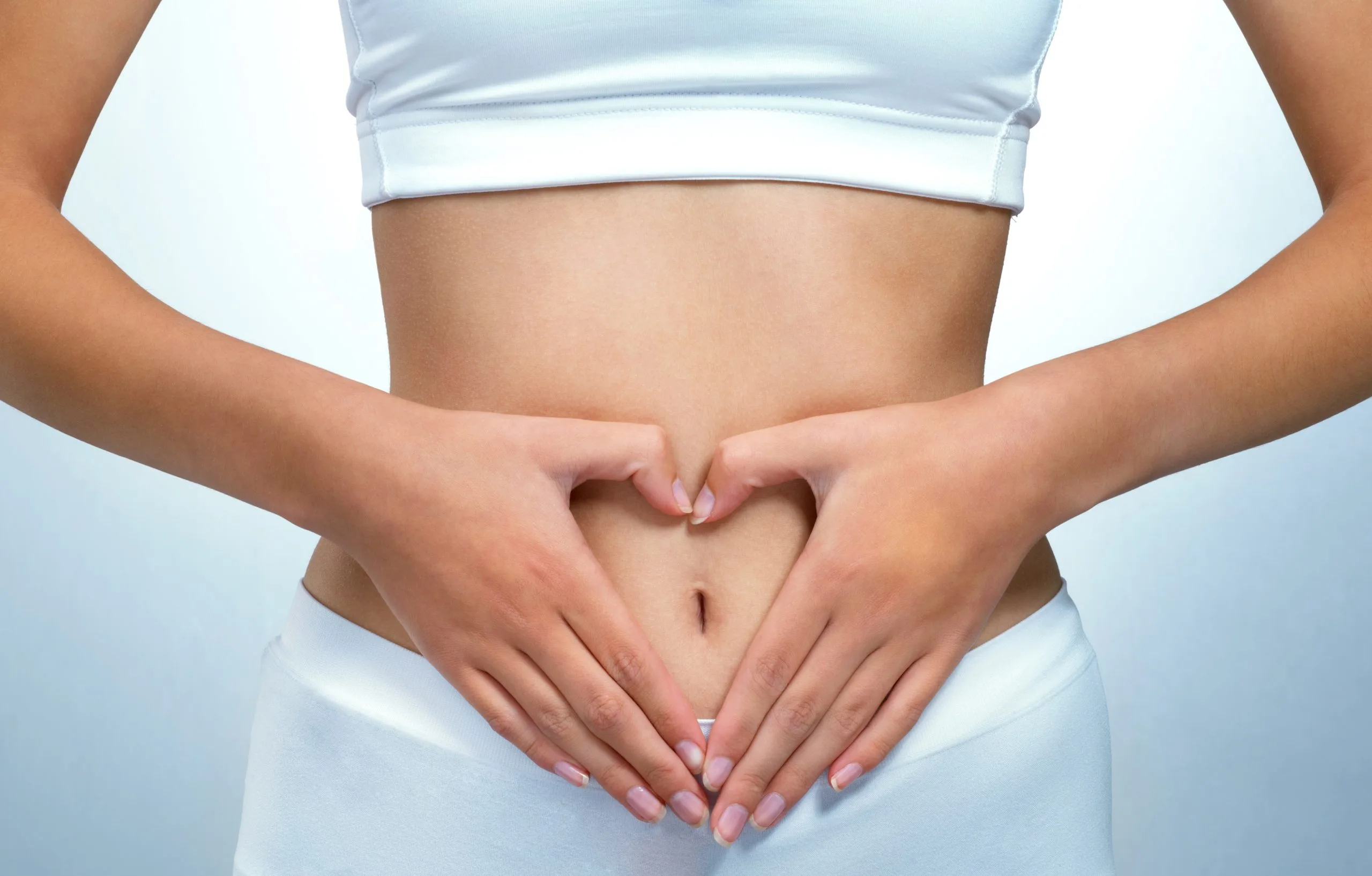Woman in white sports bra forming heart shape with hands over abdomen
