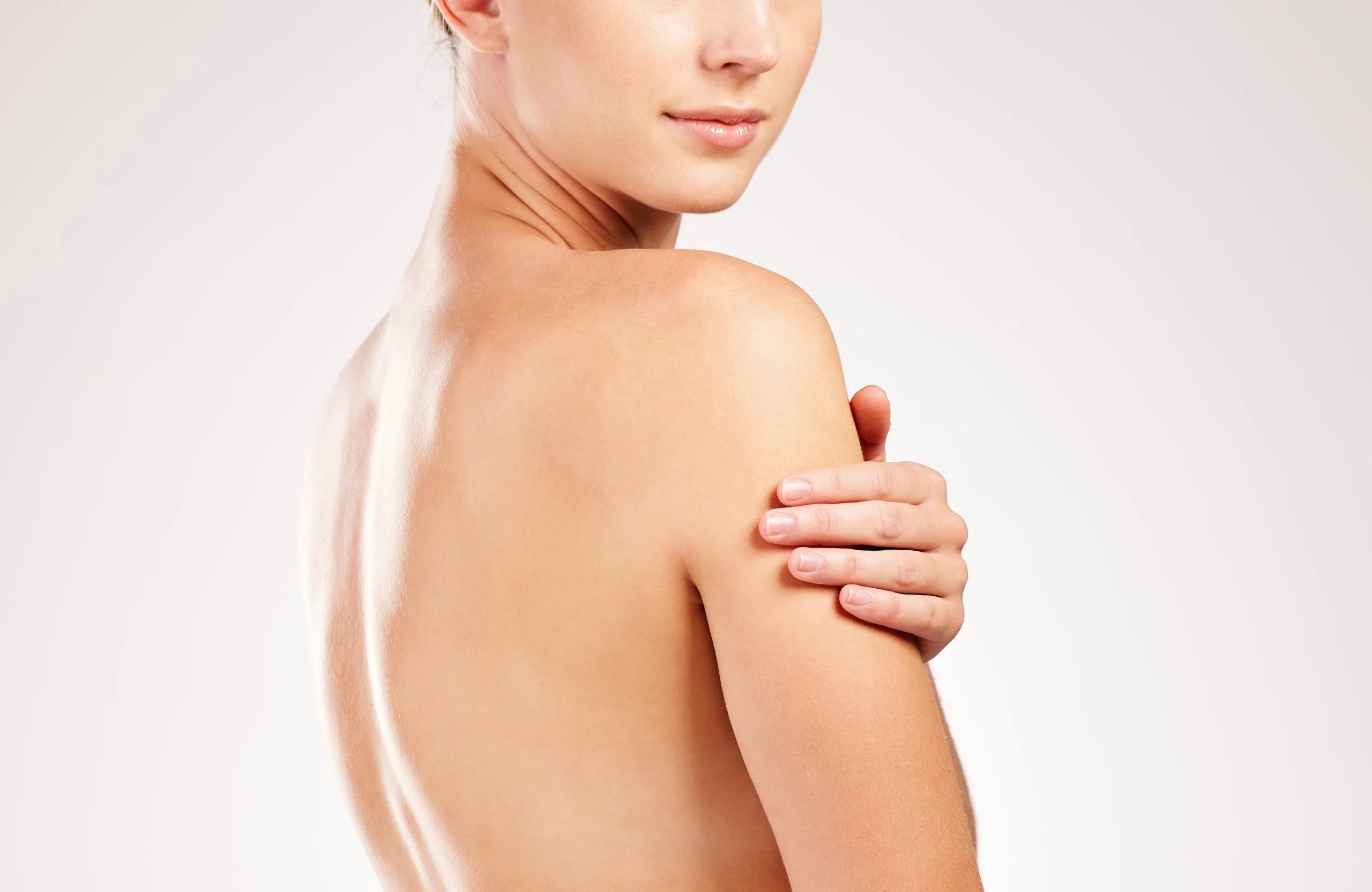 Woman touching her shoulder, shown from behind in profile against neutral background