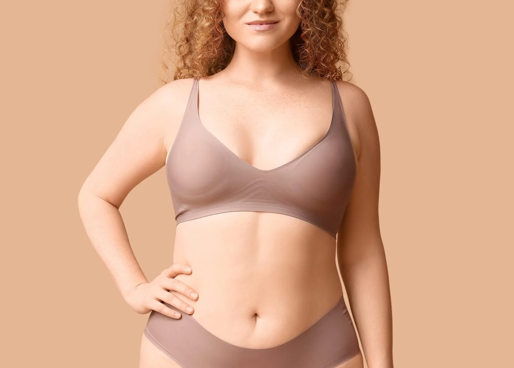 Woman wearing mauve sports bra posing against neutral background