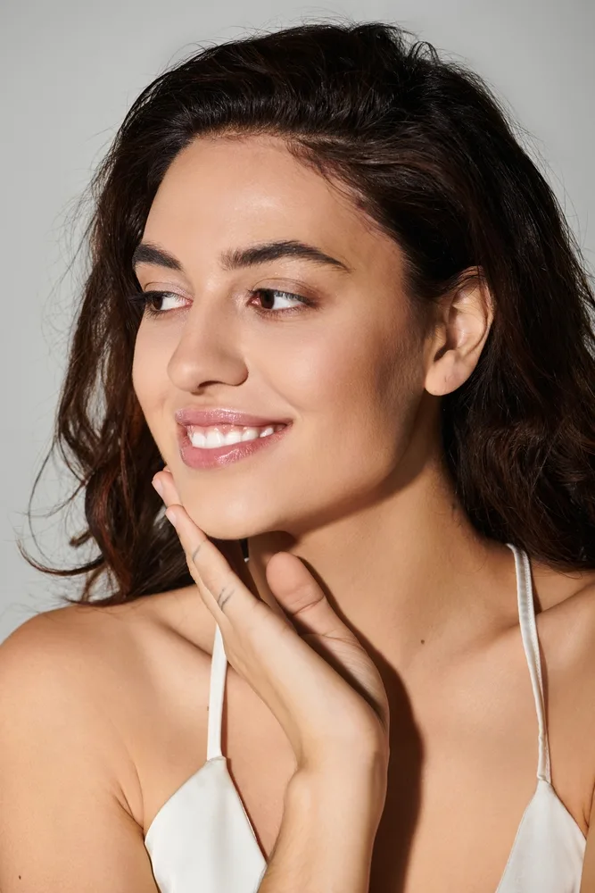 Woman with dark wavy hair smiling and touching her face with her hand